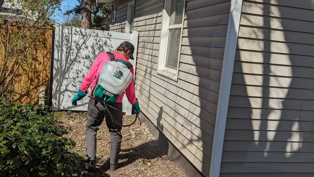 ALP technician in a pink shirt with a backpack sprayer treating the foundation of a house